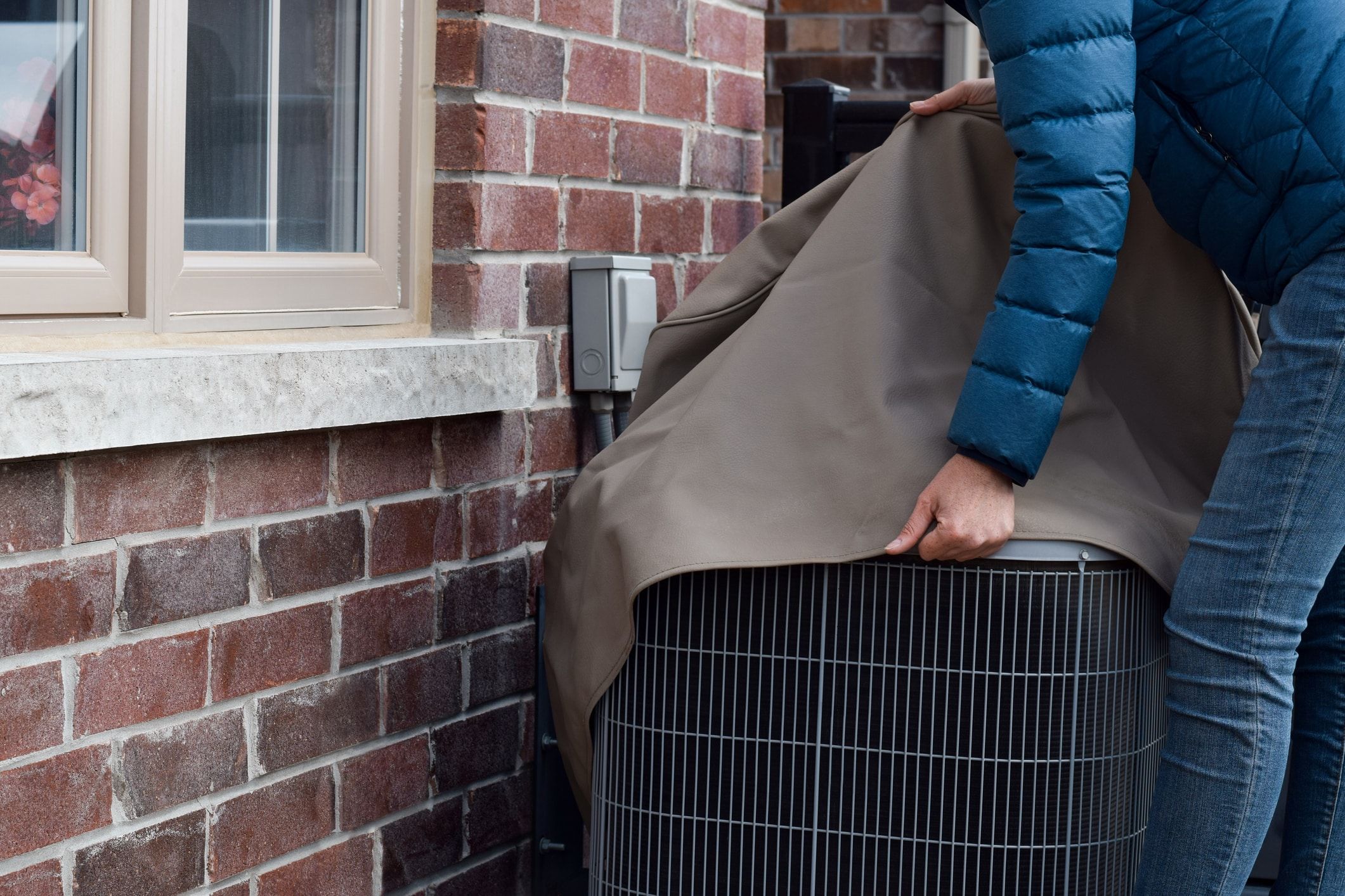 Close view of a person in a winter jacket putting a cover over their outdoor AC unit. Close view of a person in a winter jacket putting a cover over their outdoor AC unit.