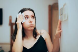 Woman wiping sweat from her forehead while checking a thermostat