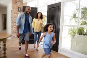 Mother, father, and young daughter walking inside their house, smiling.